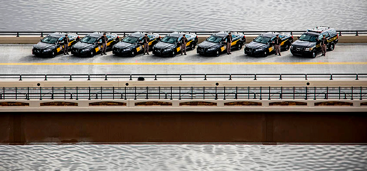 An aerial photograph of several Ottawa County officers lined up next to their cruisers as they stand at attention on the US-231 Bypass bridge